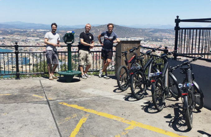 Three men with bicycles at a scenic overlook with mountains in the background on Gibraltar ebike tour.