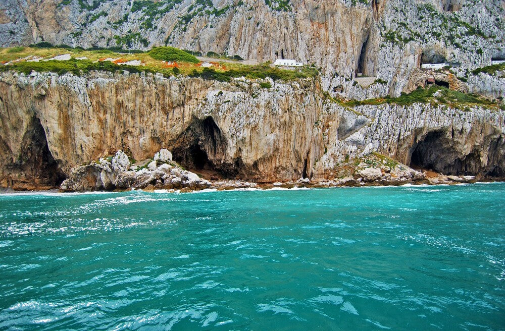 Turquoise waters near rocky cliffs off Gibraltar with greenery