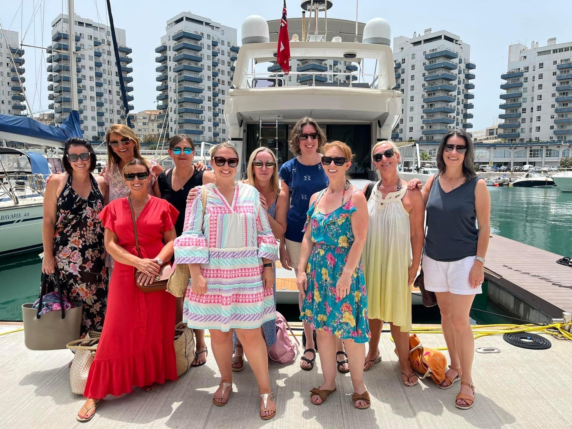 Group of women posing in front of a yacht with buildings and water in the background