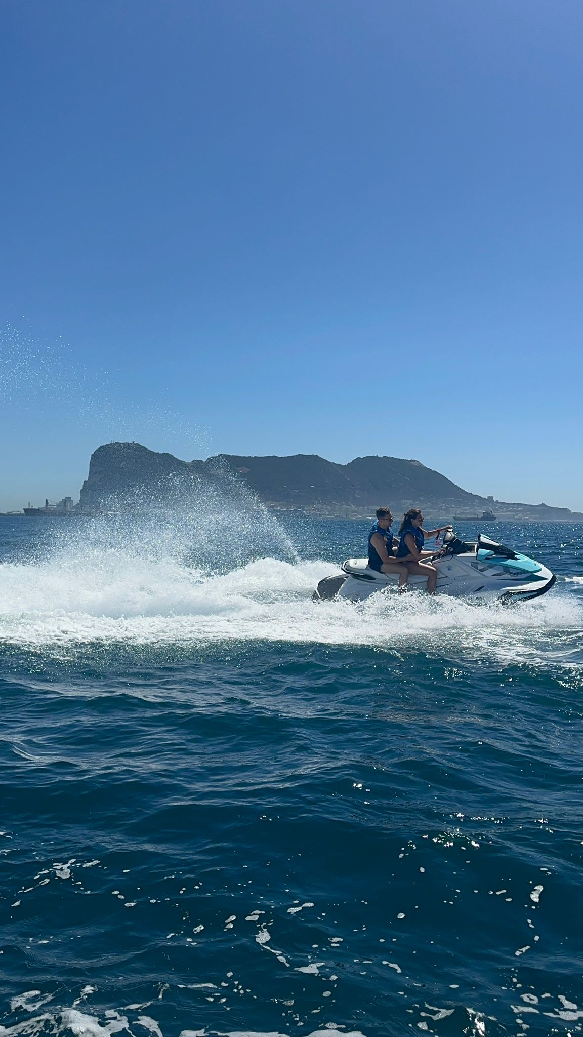 Two people on a jet ski in the ocean with a mountainous island in the background.