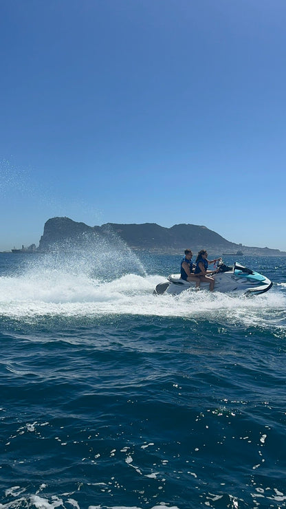 Two people on a jet ski in the ocean with a mountainous island in the background.