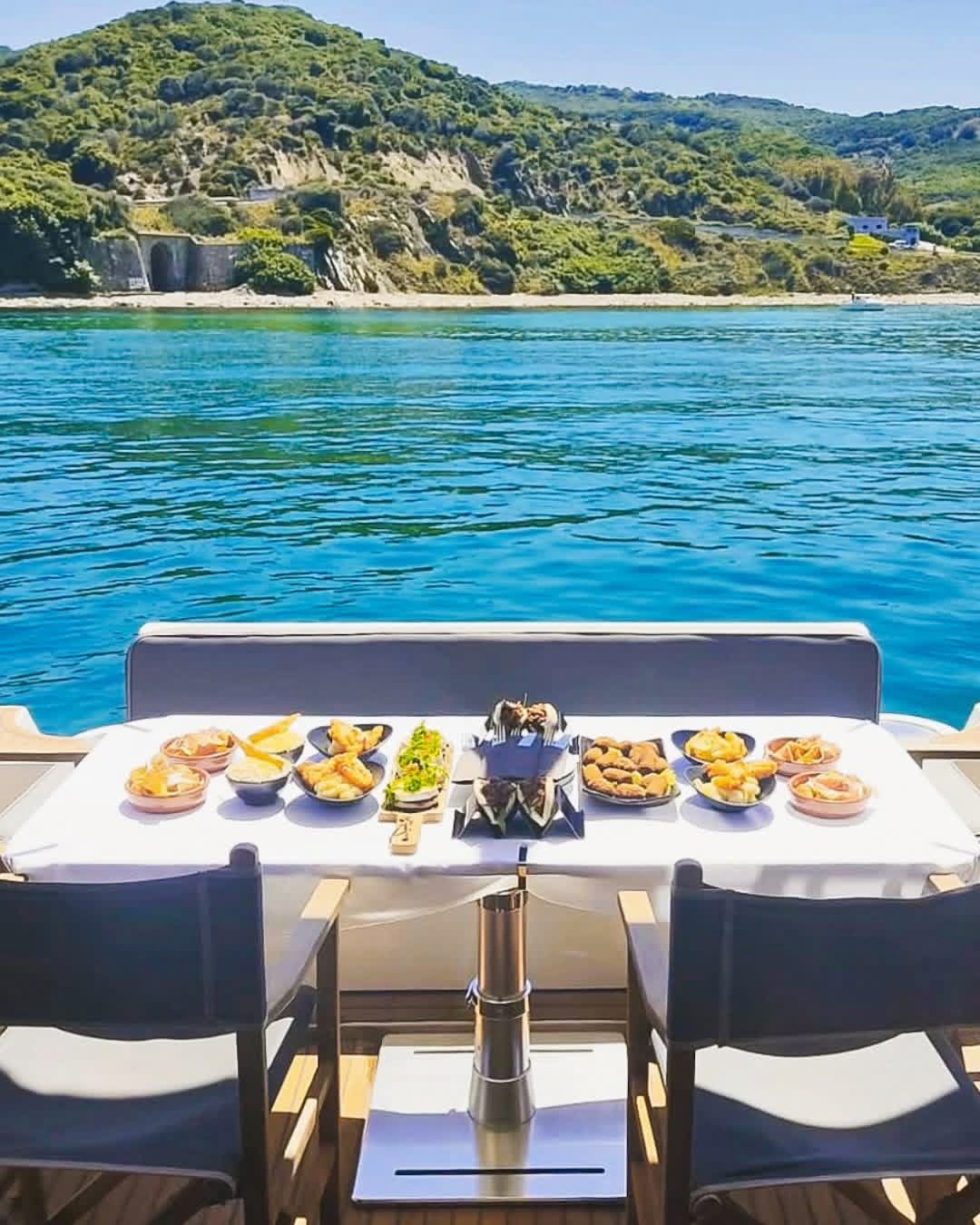 Table with food on a boat with a scenic view of water and mountains.