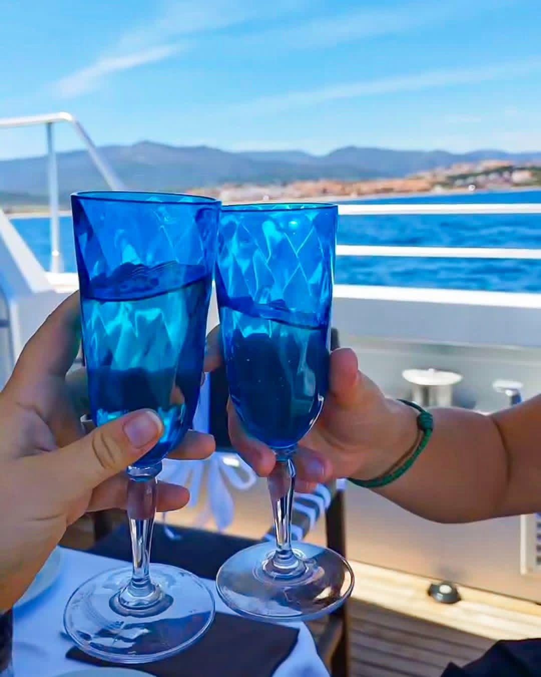 Two people clinking blue glasses on a yacht with a scenic background