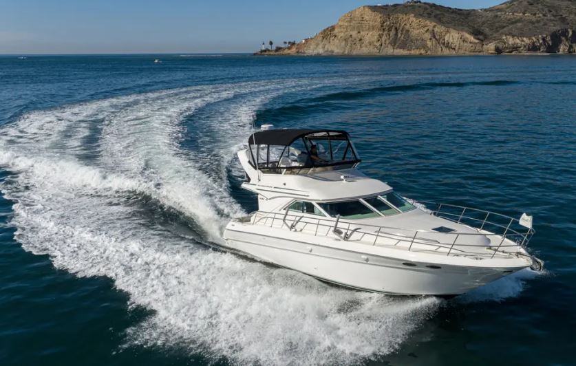 White yacht speeding on the ocean with a mountainous coastline in the background