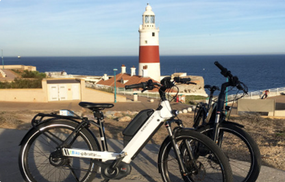 Two electric bikes parked on a path with Gibraltar lighthouse in the background.