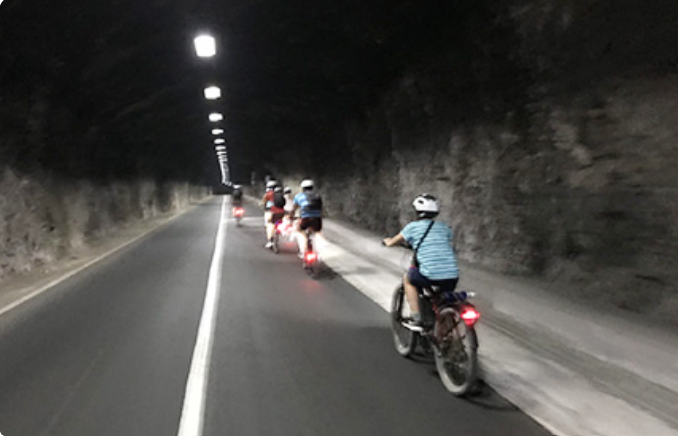 Group of cyclists riding on a dark road with streetlights lining the tunnel.