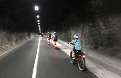 Group of cyclists riding on a dark road with streetlights lining the tunnel.